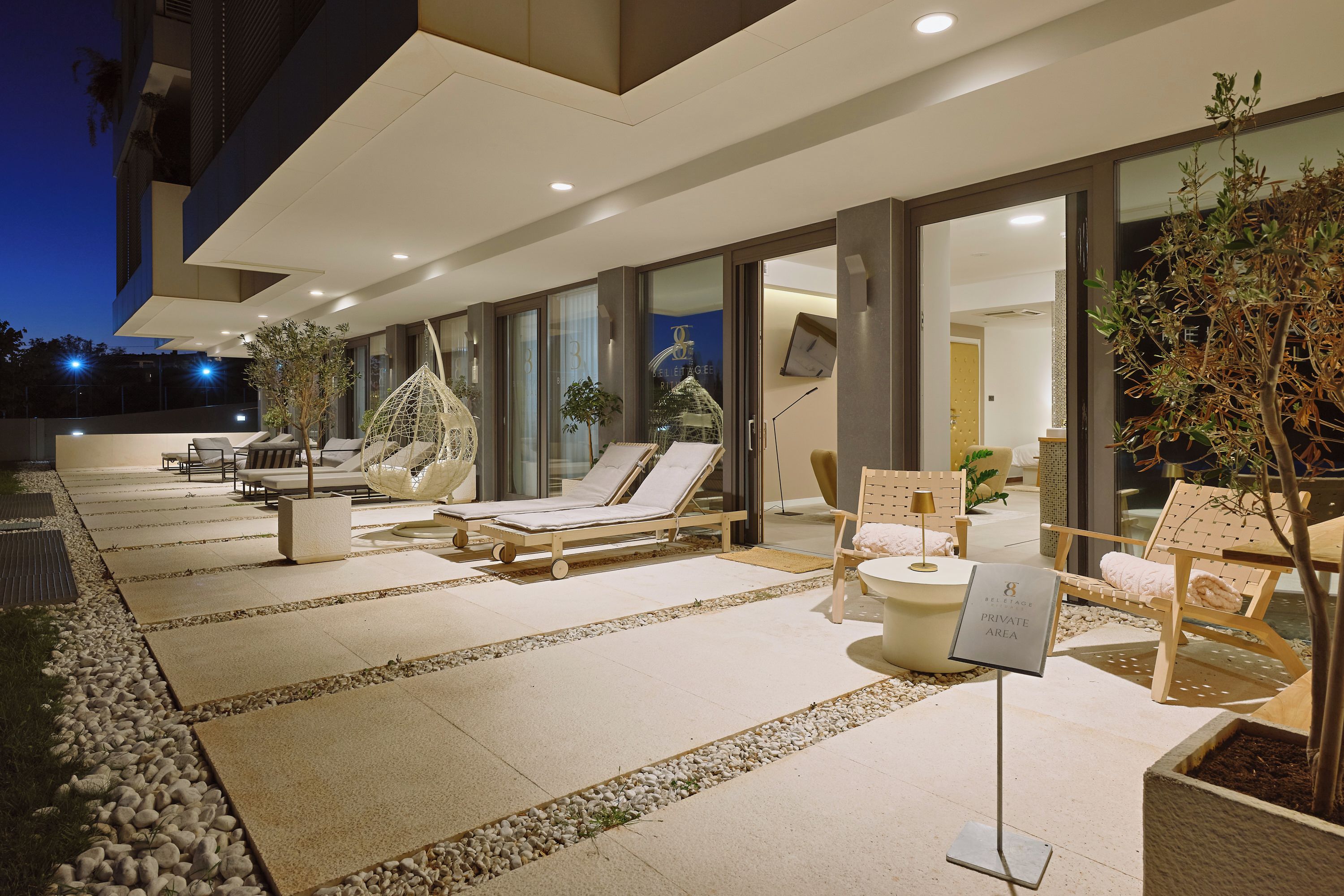A well-lit outdoor lounge area with sun loungers, a swing chair, and potted plants.