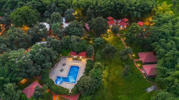 An aerial view of a resort with multiple red-roofed buildings, a swimming pool, and surrounding greenery.