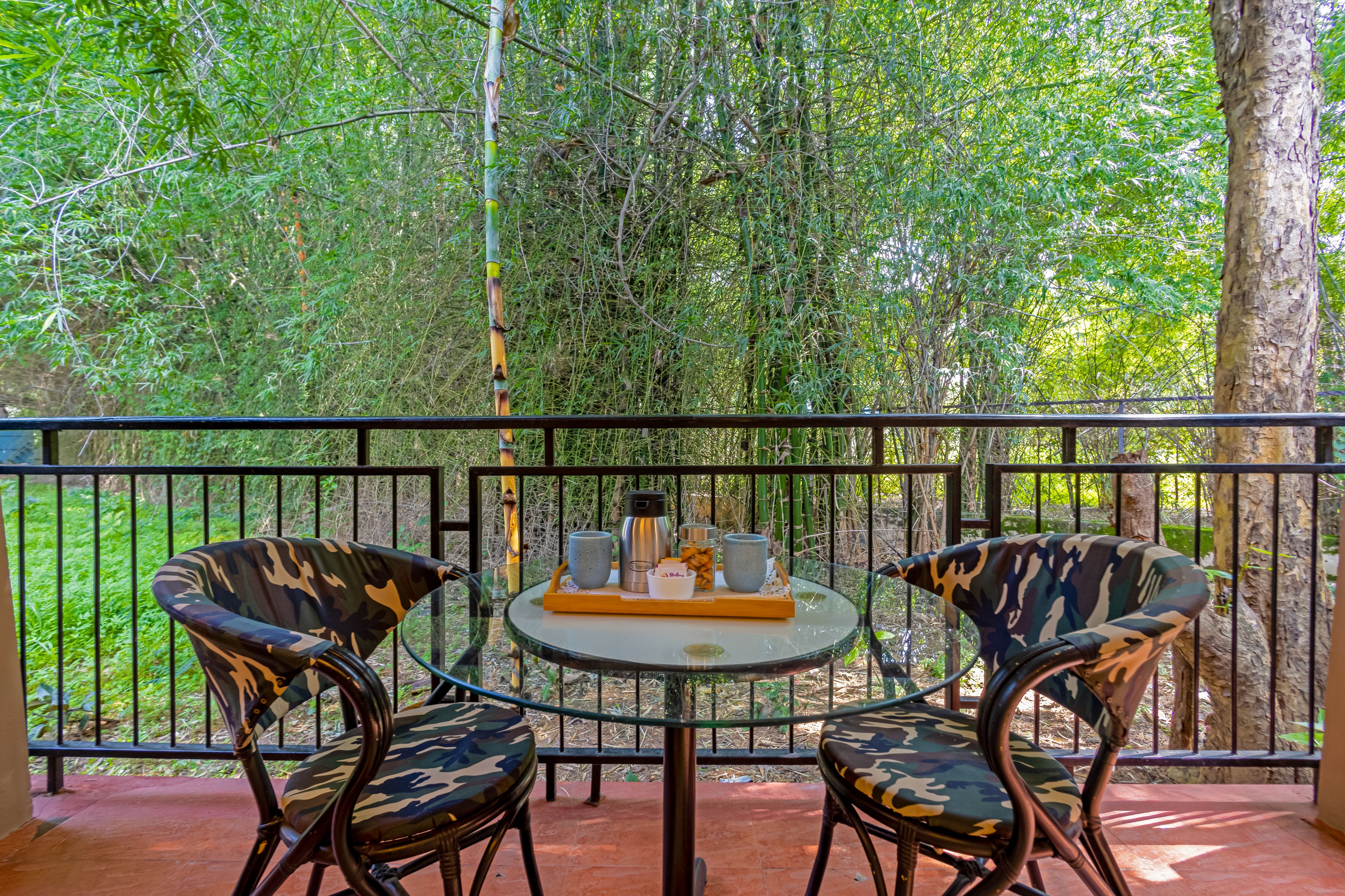 Ein Balkon mit zwei Stühlen und einem Tisch, umgeben von einer schwarzen Metallreling, mit Blick auf einen dichten, grünen Wald.