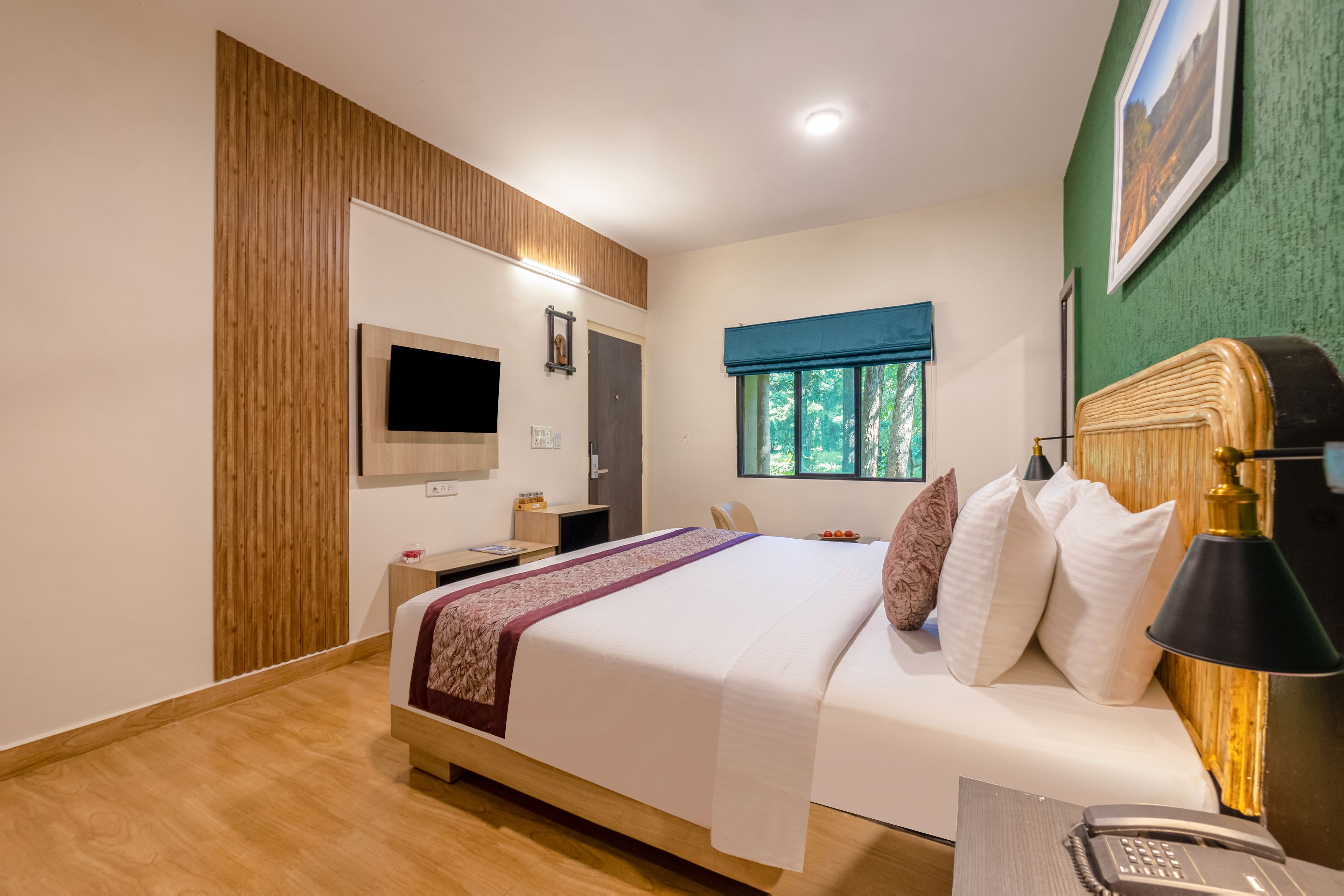 Een hotelkamer met een bed, een bureau, een televisie en een raam met uitzicht op bomen.