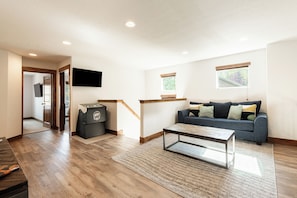 A modern living room with a wooden floor, a sofa, a coffee table, and a TV mounted on the wall. - 5BR, 4.5BA Park City retreat near Jordanelle, sleeps 18. (Hideout)