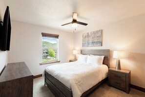 A bedroom with a bed, two bedside tables with lamps, a ceiling fan, a window with a view, and a painting on the wall. - 5BR, 4.5BA Park City retreat near Jordanelle, sleeps 18. (Hideout)
