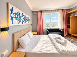 Habitación de hotel con cama, sofá, armario, ventana con cortinas y una obra de arte en la pared.