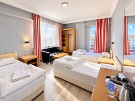 Quarto de hotel com duas camas, um sofá, uma escrivaninha e uma chaleira, e vista para a cidade.