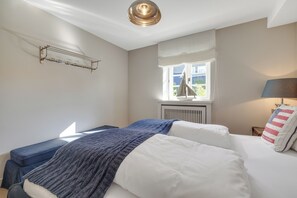Een slaapkamer met een bed, een raam, een radiator, een lamp en een wandplank.