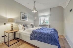 Een slaapkamer met een bed, nachtkastje, lamp, een ingelijste foto, een raam en een radiator.