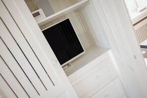Een witte kamer met een flatscreen televisie op een wit meubelstuk, een witte deur en een witte muur.