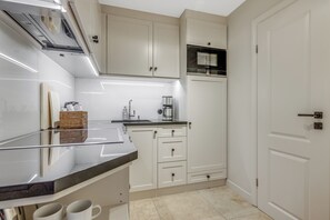 Een moderne keuken met witte kastjes, een roestvrijstalen afzuigkap, een koffiezetapparaat en een mand op het aanrecht.
