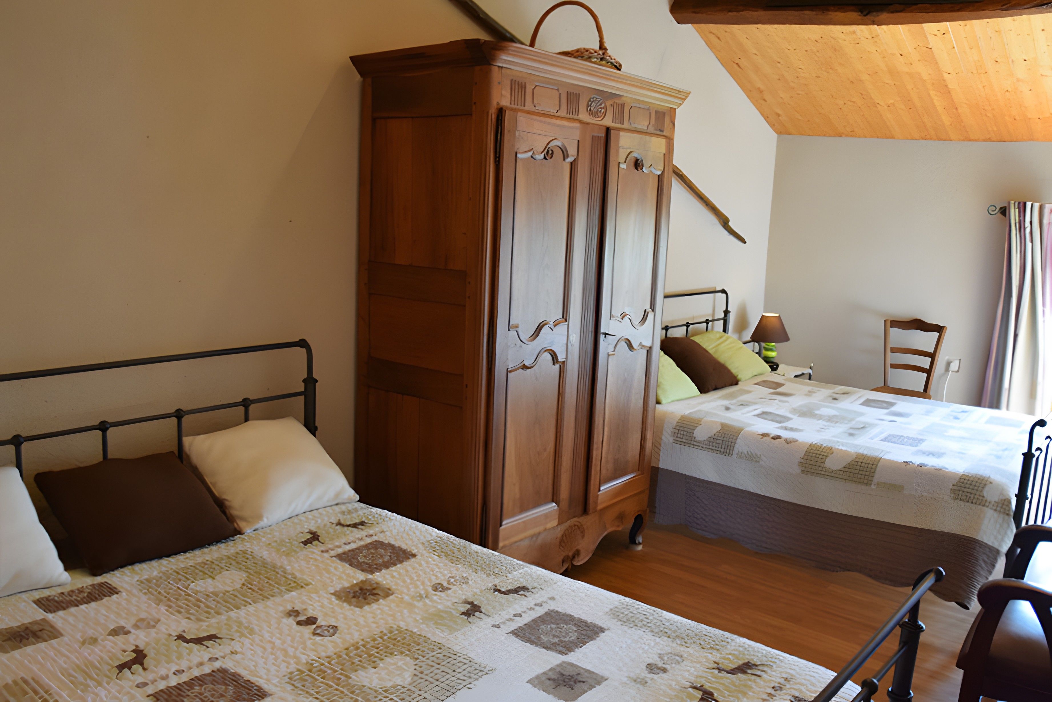 A bedroom with two beds, a wooden wardrobe, and a chair.