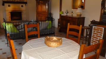 Een eethoek met een ronde tafel, stoelen, een rieten mand en een open haard.
