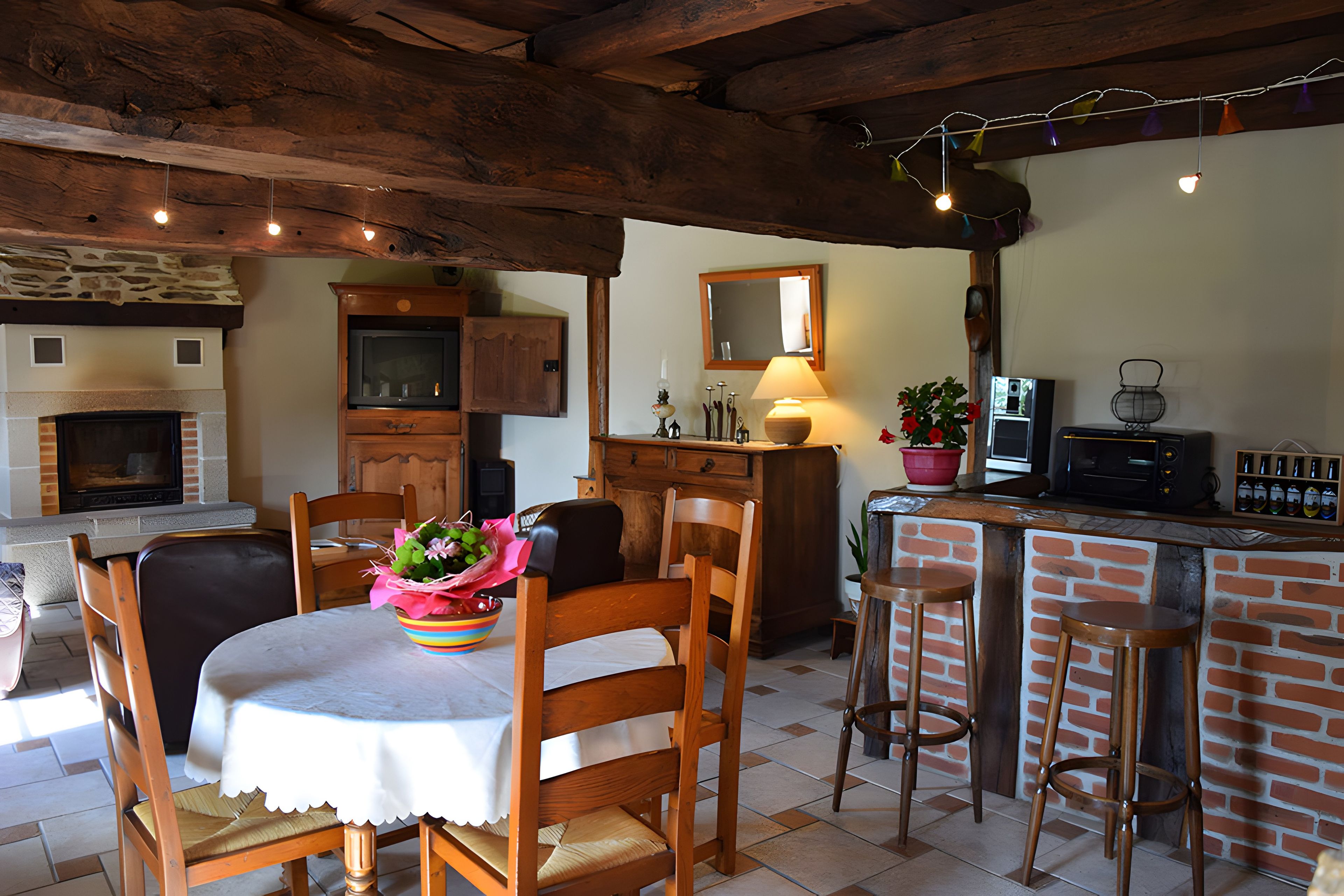 Uma área de refeições acolhedora com lareira de tijolos, cadeiras de madeira, uma mesa com toalha branca e um balcão com bancos.