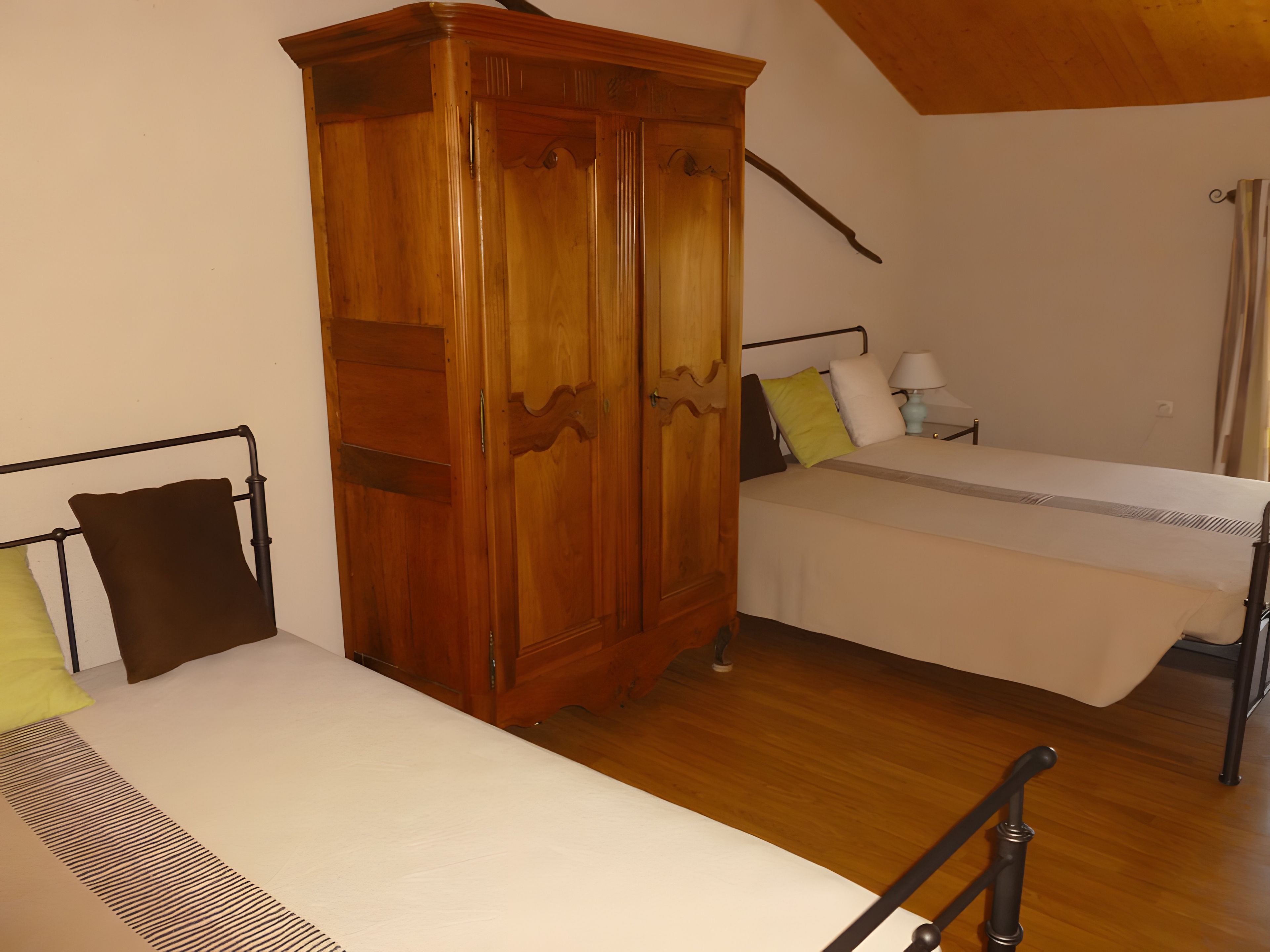 A room with two beds, a wooden wardrobe, and a nightstand with a lamp.