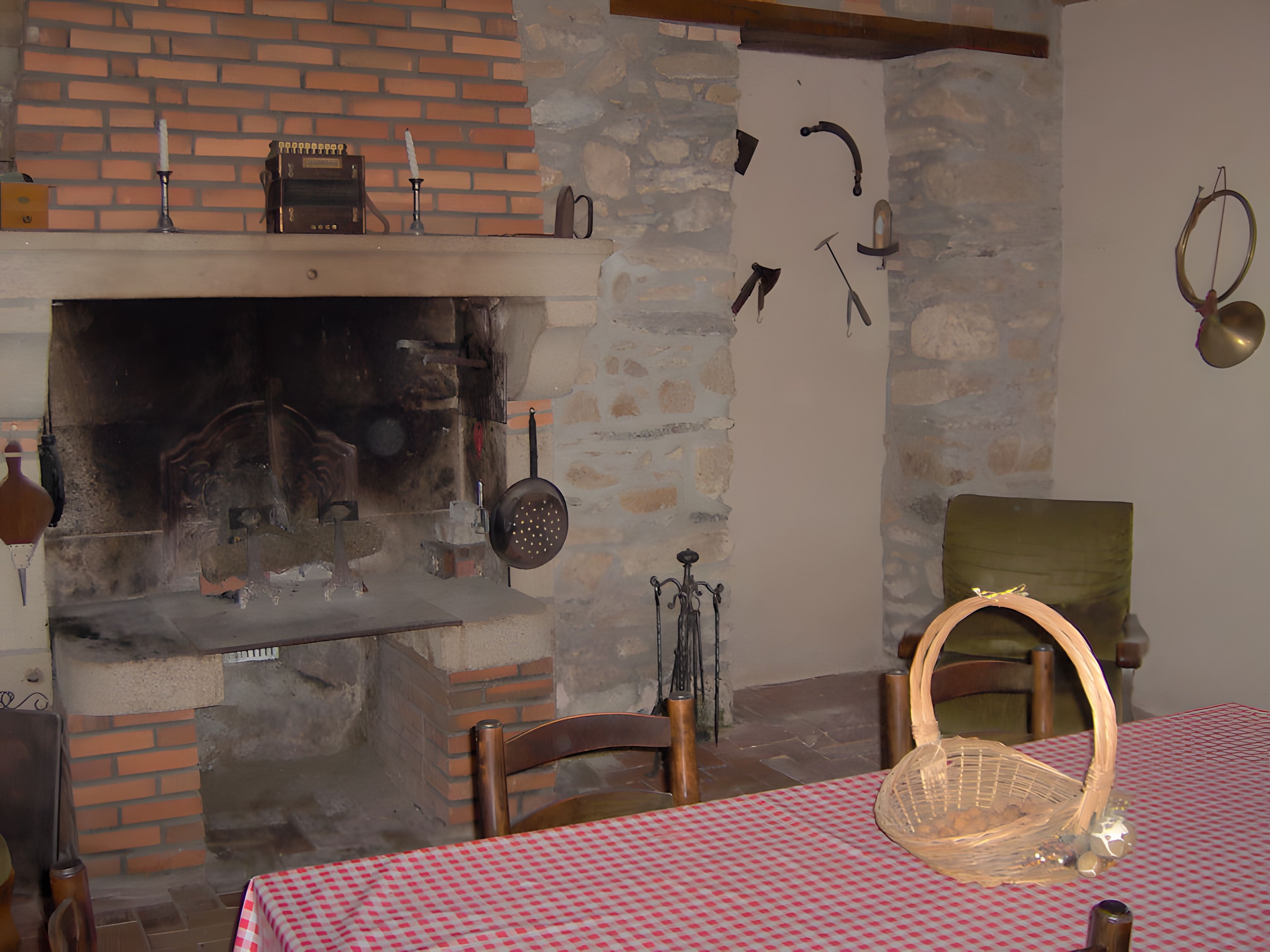 A rustic kitchen with a brick oven, hanging utensils, and a checkered tablecloth.