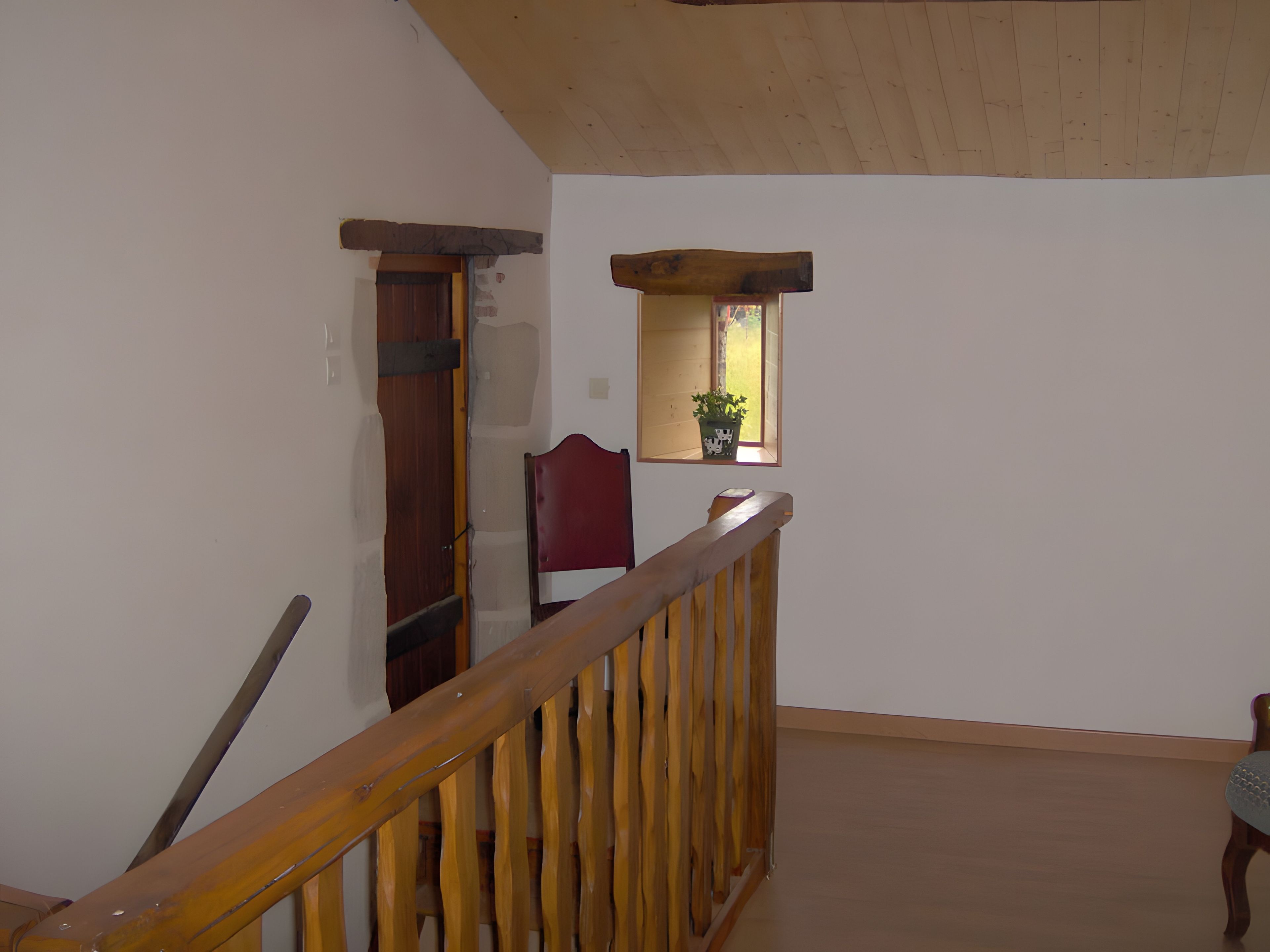 Un escalier en bois, doté d’une rampe, mène à un palier. On aperçoit une porte en bois et une chaise au fond.