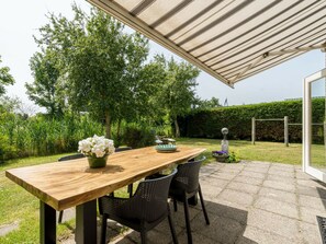 An outdoor patio with a wooden table, black chairs, and a covered area. - Holiday Home With 3 Bedrooms (Burgh-Haamstede)