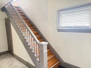 A staircase with wooden steps and white balusters, leading to a landing with a window with blinds. - 3-bedroom house in peaceful Niagara Falls with AC comfort (Niagara Falls)
