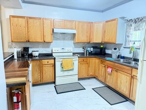 A kitchen with wooden cabinets, a white stove, a microwave, and a sink. - 3-bedroom house in peaceful Niagara Falls with AC comfort (Niagara Falls)