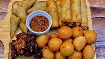 A wooden tray with various fried snacks, including samosas, spring rolls, and fried dough balls, accompanied by a bowl of chutney.