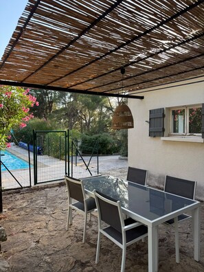 Eine Terrasse im Freien mit Glastisch und -stühlen, einem Pool und einem überdachten Bereich mit Bambusdach.