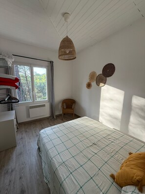 Ein Schlafzimmer mit einem Bett, einem Sessel, einer Pendelleuchte und einem Fenster.