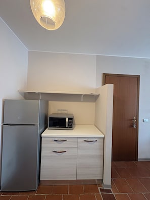 Una cocina compacta con refrigerador, microondas y una puerta de madera.