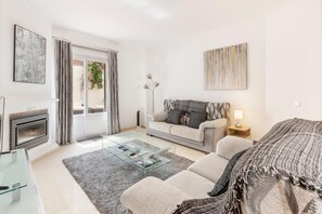 Un salon moderne avec une table basse en verre, un canapé, une cheminée et une grande fenêtre avec des rideaux.