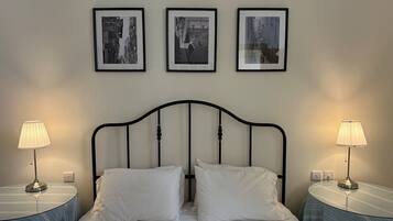 A neatly made bed with two pillows, flanked by two bedside tables with lamps, in a room with three framed pictures on the wall.
