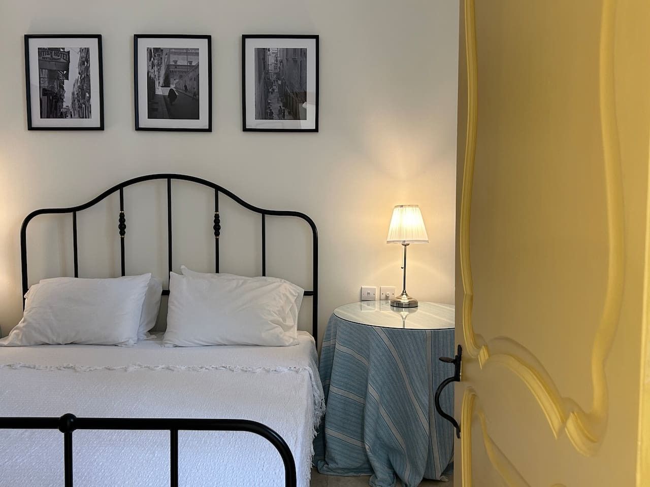 Ein Bett mit weißer Bettwäsche, ein Nachttisch mit Lampe und drei gerahmte Bilder an der Wand.