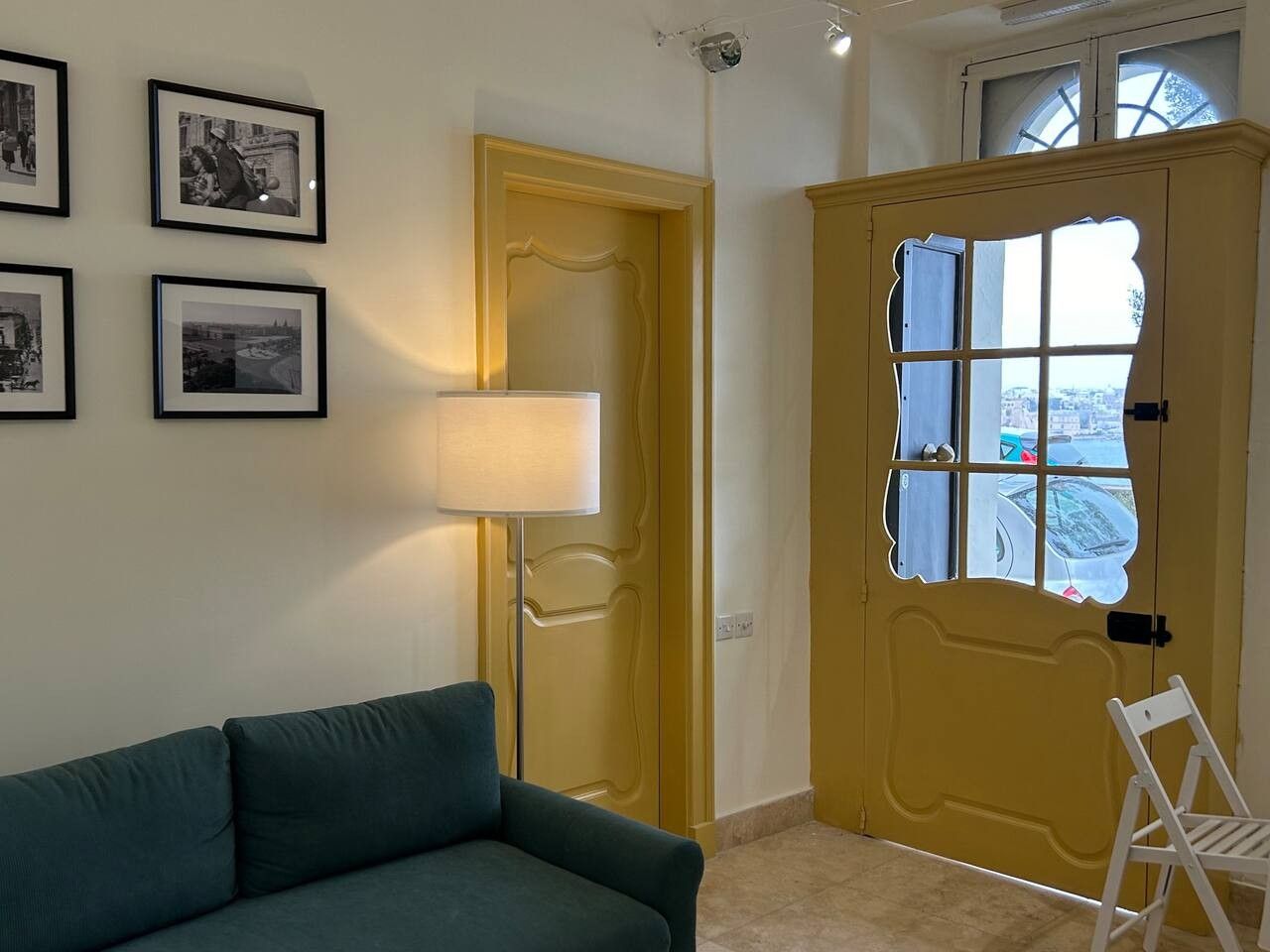 A room with a green sofa, a lamp, a yellow door with a window, and framed pictures on the wall.