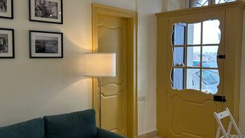 A room with a green sofa, a lamp, a yellow door with a window, and framed pictures on the wall.