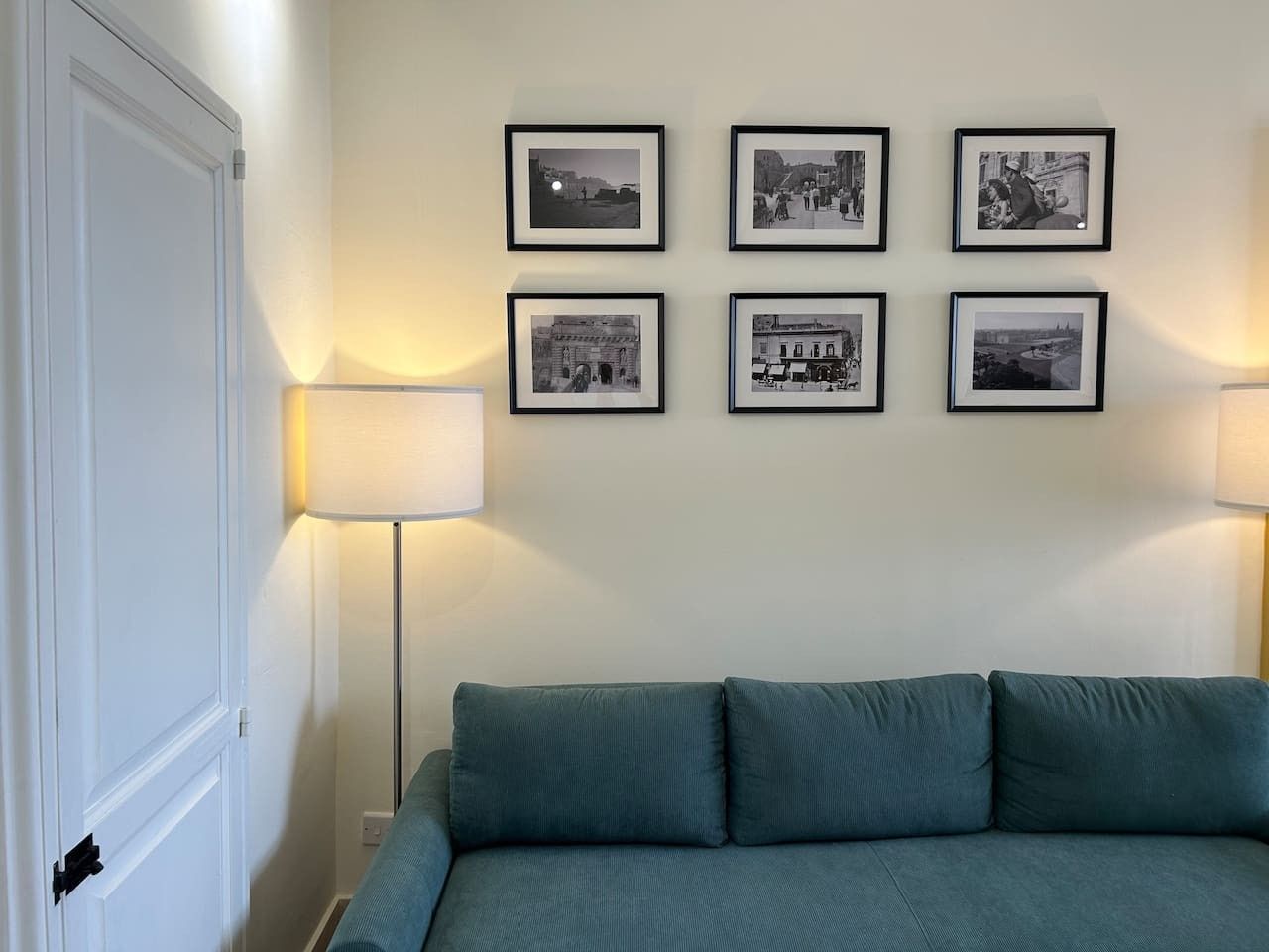 A room with a bed, a door, and six framed photographs on the wall.