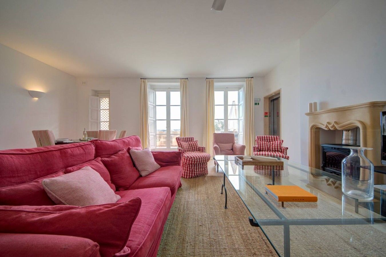 A living room with a red sofa, checkered chairs, a glass coffee table, and a fireplace.