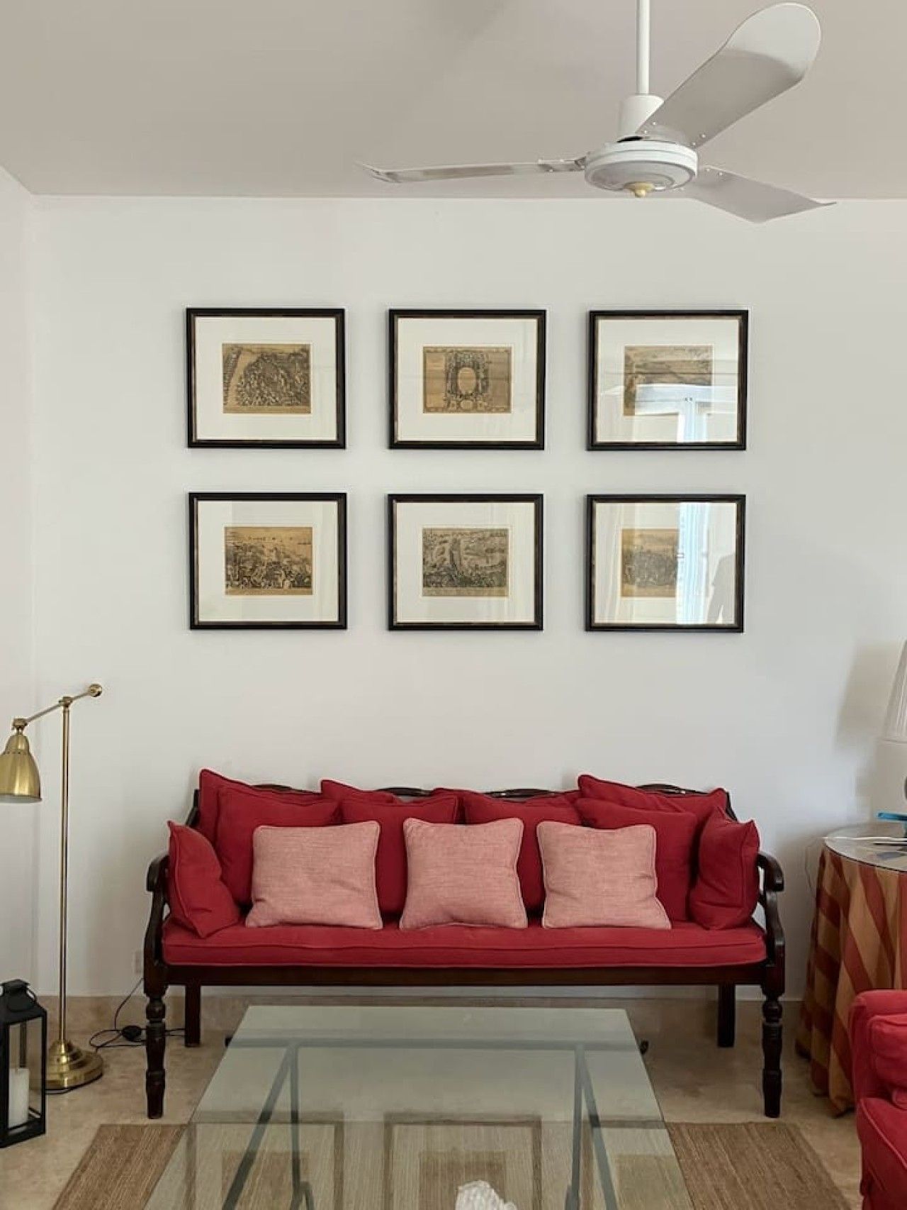 A living room with a red sofa, a glass coffee table, and six framed pictures on the wall.