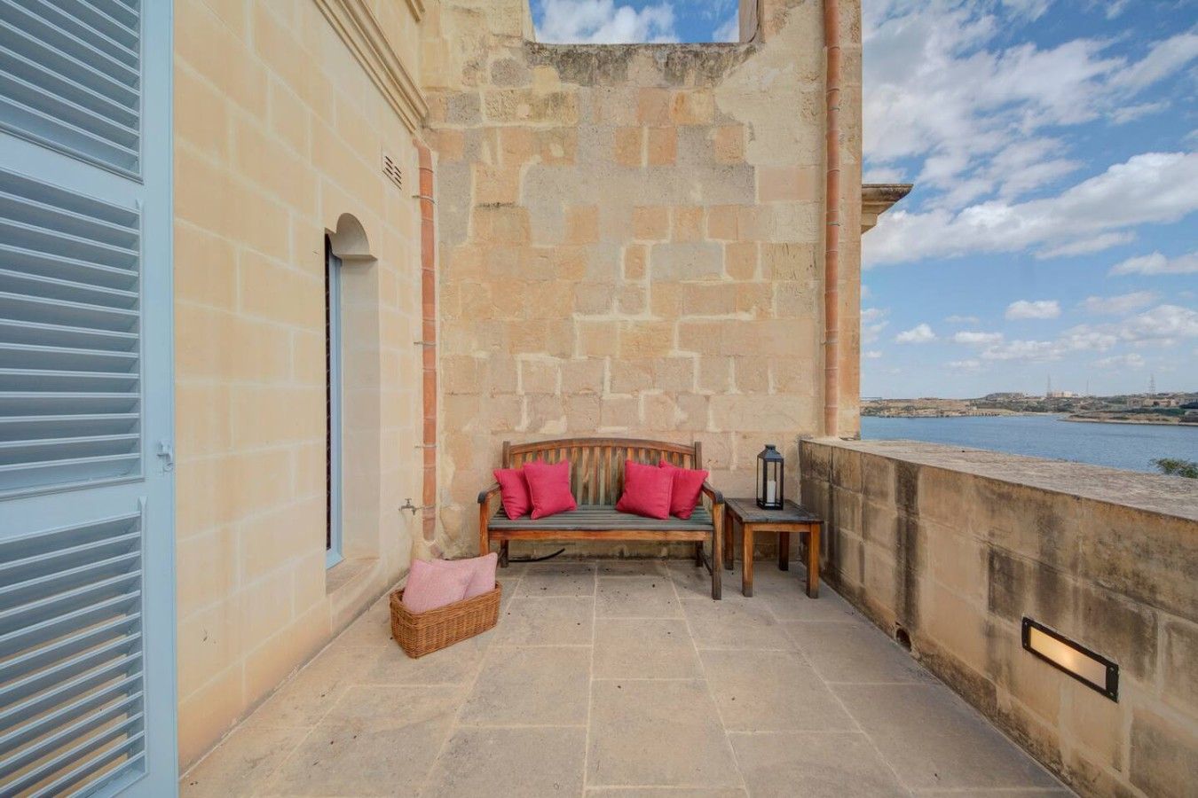 A stone-walled balcony with a wooden bench, a wicker basket, and a lantern.