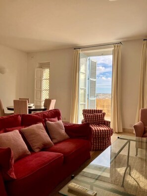 A living room with a red sofa, a striped armchair, and a glass coffee table. - Penthouse w/ unique harbour view (Il-Belt Valletta)