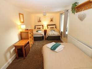 A hotel room with two beds, a wooden dresser, a desk, a hanging plant, and a radiator. - Gap Farm (Brampton)
