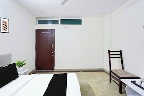 A hotel room with a bed, a chair, a desk, a potted plant, and a door.