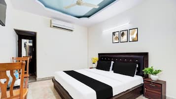 Une chambre à coucher comprenant un lit, un ventilateur de plafond, un appareil de climatisation, une table de chevet avec une plante et une œuvre d’art accrochée au mur.