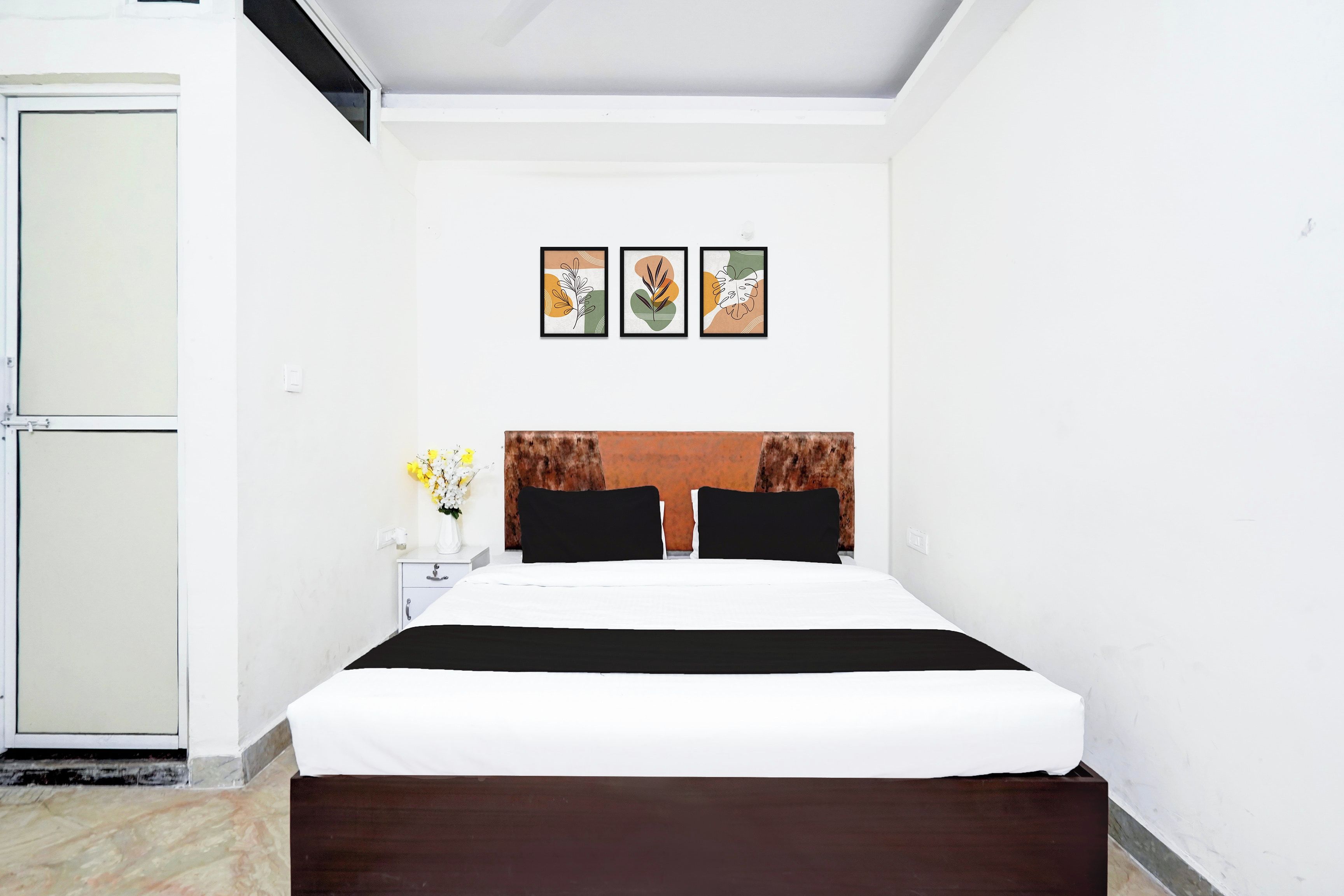 Une chambre d’hôtel avec un lit, une table de chevet ornée d’un vase de fleurs et trois œuvres d’art encadrées accrochées au mur.