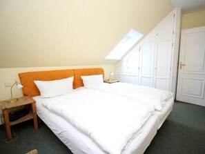 A bedroom with a bed, a nightstand, a lamp, a wardrobe, and a skylight. - Villa Mowe Holiday Apartment D (Sylt)