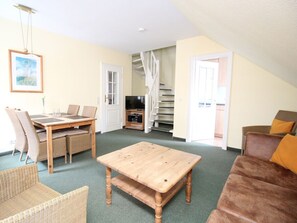A living room with a wooden coffee table, wicker furniture, a sofa, and a television. - Villa Mowe Holiday Apartment D (Sylt)