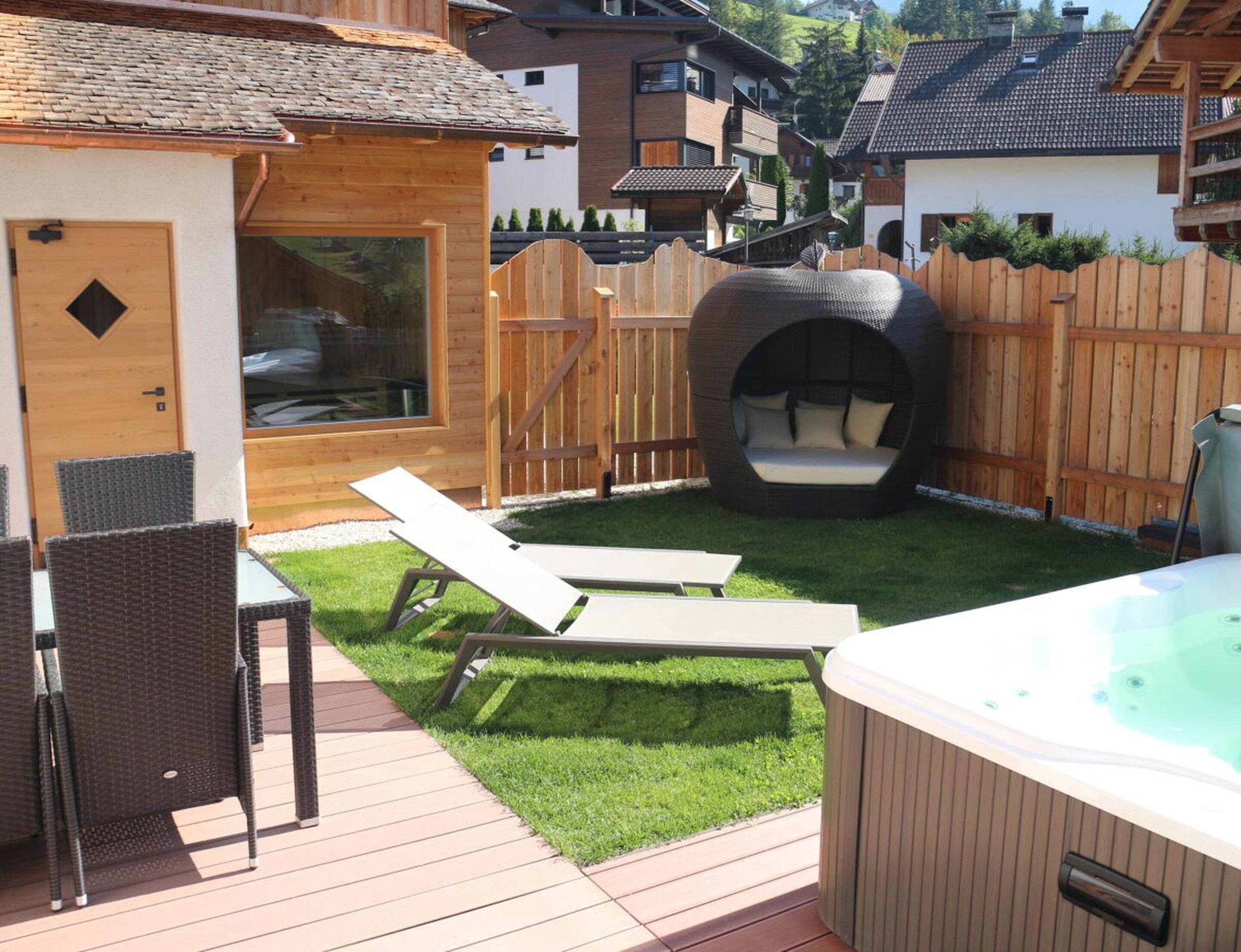 A wooden deck with two lounge chairs, a hot tub, and a wooden playhouse with a window.
