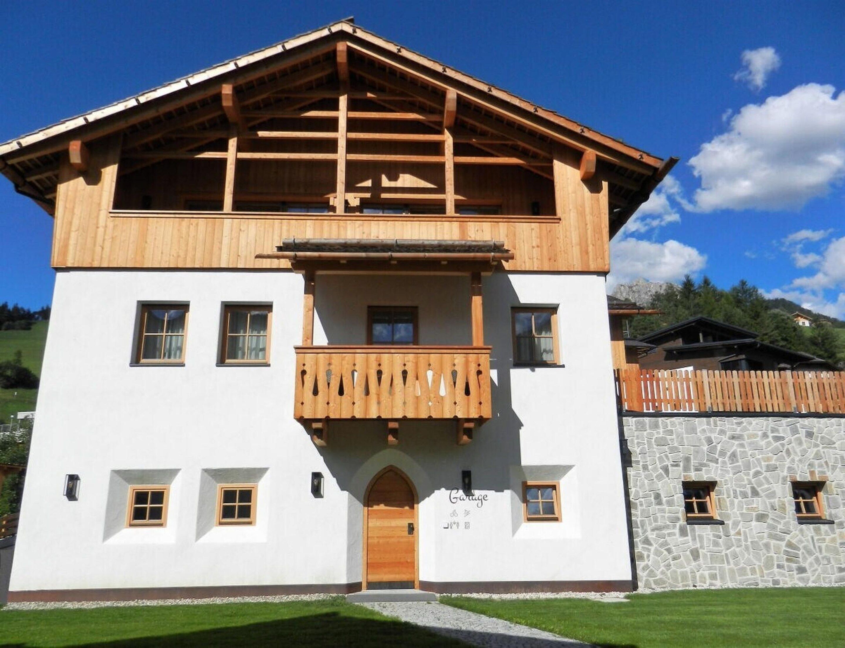 A two-story building with a wooden balcony, a garage entrance, and a stone wall.