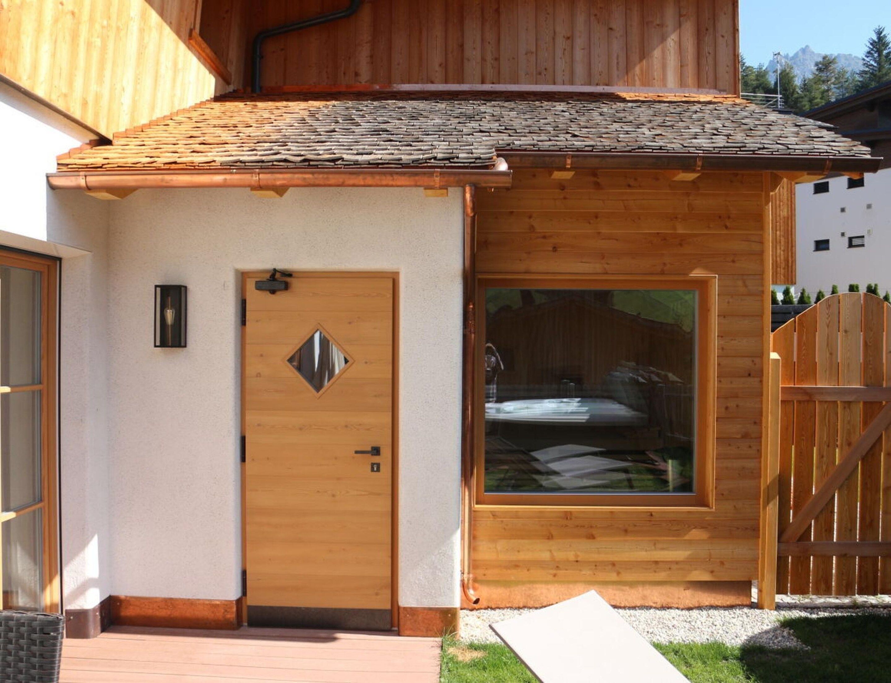 A wooden cabin with a large window, a door with a diamond-shaped window, and a wooden fence.