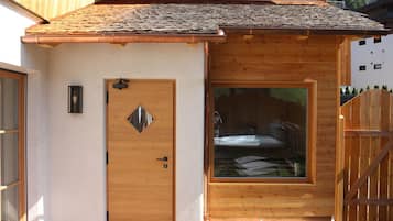 A wooden cabin with a large window, a door with a diamond-shaped window, and a wooden fence.