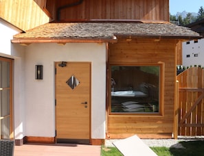 A wooden cabin with a large window, a door with a diamond-shaped window, and a wooden fence. - Liondes Chalet Moltina (Marebbe)
