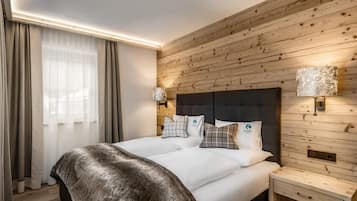 A modern hotel room with a wooden wall panel, a large bed with white bedding, two bedside lamps, and a small bedside table.