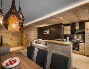 A modern kitchen with wooden cabinetry, a dining area with a wooden table and chairs, and a cozy seating area with a sofa. - Liondes Chalet Moltina (Marebbe)