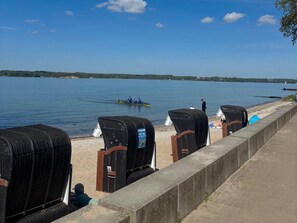 A waterfront view with a row of wicker lounge chairs and a rowboat on the water. - Holiday Apartment With 1 Bedroom (Gluecksburg)