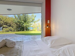 A bedroom with a bed, pillows, a lamp, and a view of a garden. - Beautiful villa, ocean view, pool, beach within walking distance (Corbara)